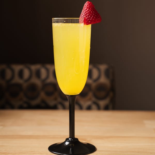 A mimosa in a flute glass with a strawberry garnish sits on a wooden table.