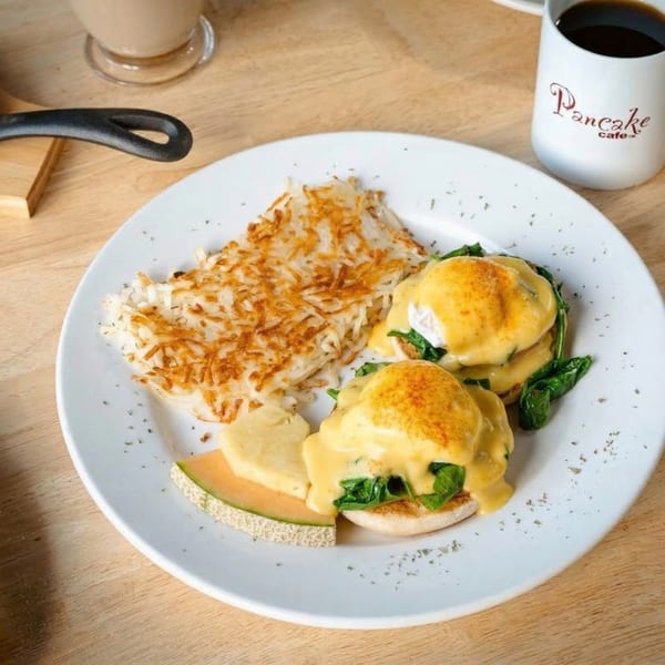 Eggs Benedict with hash browns and melon, alongside a Pancake Cafe coffee mug.