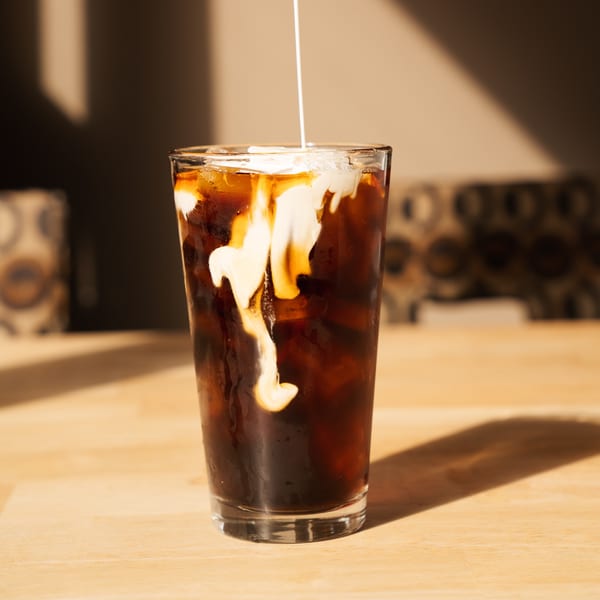 Cream being poured into a glass of iced coffee on a wooden table at Pancake Cafe.