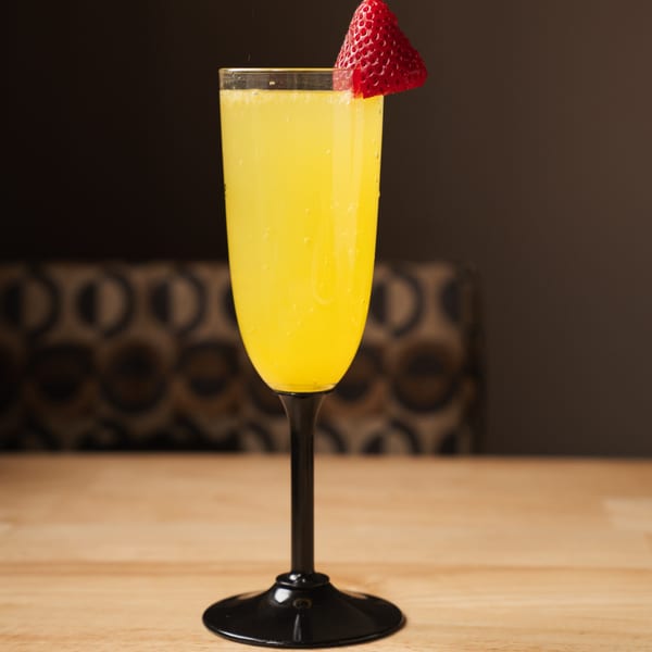 A mimosa in a flute glass with a strawberry garnish sits on a wooden table.