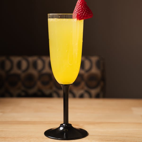 A mimosa in a flute glass with a strawberry garnish on a wooden table at Pancake Cafe.