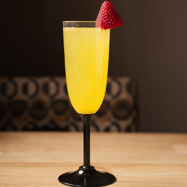 A mimosa in a tall glass with a black stem, garnished with a fresh strawberry.