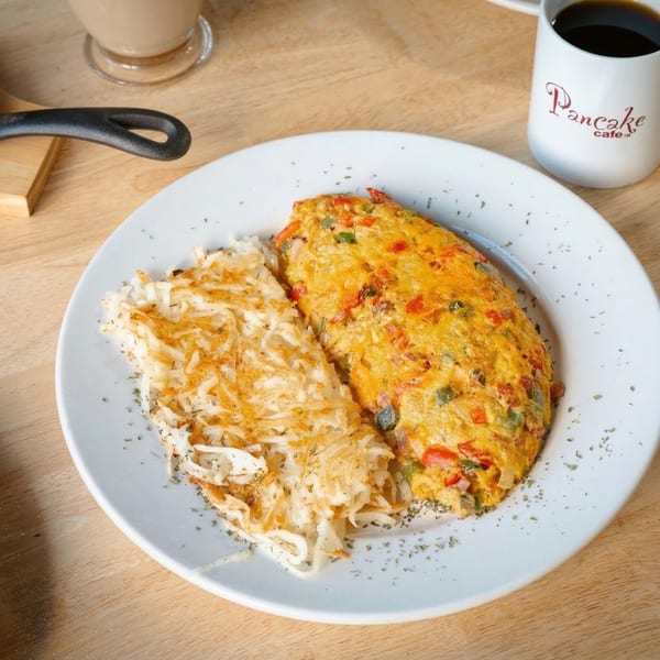 A fluffy omelet with hash browns on a white plate, with a Pancake Cafe coffee mug.